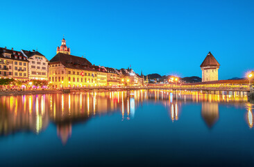 Fototapeta premium Beautiful view of Lucerne, Switzerland featuring the famous wooden Chapel Bridge with Water Tower over the Reuss River. Scenic cityscape with alpine mountains, clear water, and colorful historic archi