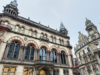 Naklejka premium Historic Manchester architecture with ornate arched windows and towers along a bustling street in city center