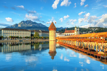 Fototapeta premium Beautiful view of Lucerne, Switzerland featuring the famous wooden Chapel Bridge with Water Tower over the Reuss River. Scenic cityscape with alpine mountains, clear water, and colorful historic archi