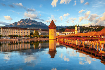 Fototapeta premium Beautiful view of Lucerne, Switzerland featuring the famous wooden Chapel Bridge with Water Tower over the Reuss River. Scenic cityscape with alpine mountains, clear water, and colorful historic archi