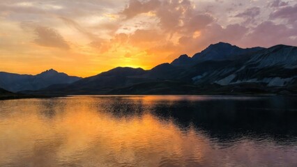 Obraz premium Mountain silhouettes mirrored in lake during colorful sunset.