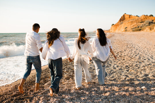 Happy family with two kid girls running at beach over sea outdoors. Summer vacation season. Parenthood.