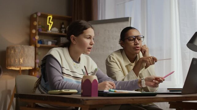 Medium shot of Caucasian student sitting at desk and asking tutor question about math task