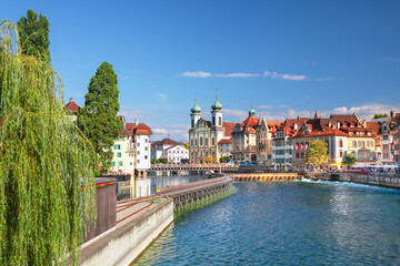 Fototapeta premium Beautiful view of Lucerne, Switzerland featuring the famous wooden Chapel Bridge with Water Tower over the Reuss River. Scenic cityscape with alpine mountains, clear water, and colorful historic archi