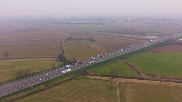 Highway Traffic Jam: An aerial view captures a long line of cars and trucks stuck in a traffic jam on a multi-lane highway, surrounded by rural farmland.