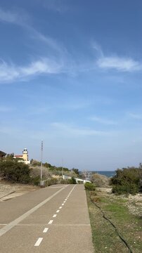 a bike path with a lighthouse and the sea in the background, with a blue sky and clouds