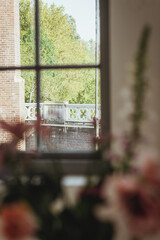 Fototapeta premium Window view, vertical image of an old vintage window framed by unfocused blooming flowers inside a house with natural light and space for text.
