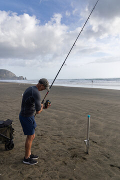 Auckland, New Zealand: A fisherman prepares his fishing rod on the beach at Piha. He is preparing to cast his line into the ocean to catch fish for food.