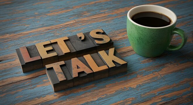 Retro letterpress printing blocks spelling out Lets Talk next to a green coffee cup on a rustic wooden table surface