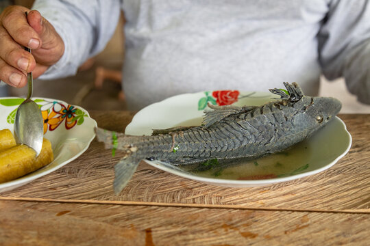 Amazonian man eating traditional carachama fish soup (armored catfish) in a rustic kitchen in the Peruvian rainforest