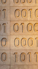 Binary code of zeros and ones carved as a bas-relief on natural stone cladding. Strict lines and order symbolize low-level programming and fundamental education.