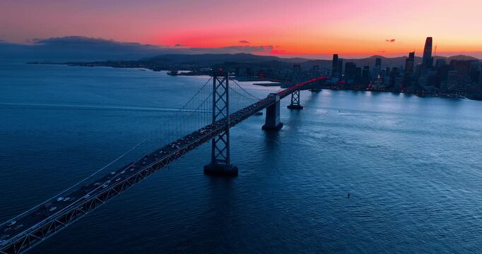 Approaching the Oakland Bay Bridge with hectic traffic. San Francisco skyline against pink sky at sundown.