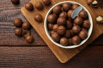 Obraz premium Macadamia nuts and metal key in bowl on wooden table, flat lay
