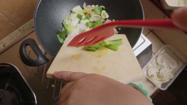 Hand Dropping Fresh sliced mustard greens and cabbage into Hot Frying Pan. Capcay or chop suey (Chinese food) cooking process. Close Up view and selective focus