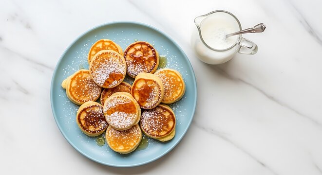 A top-down view of a plate with mini pancakes, syrup, and cream.