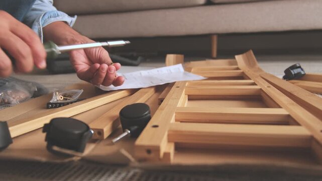 Unrecognizable person assembling flat-pack furniture at home following the instructions