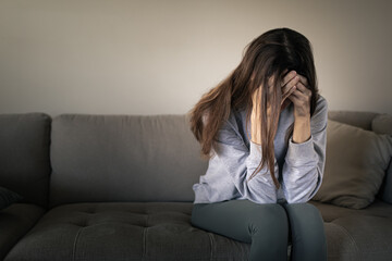 stressed woman sitting on couch covering face, anxiety and depression concept at home 