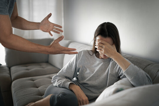 angry man shouting at upset woman on couch, domestic conflict and emotional abuse concept
