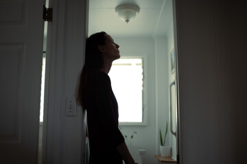 exhausted woman leaning against bathroom doorway, stress and burnout at home 