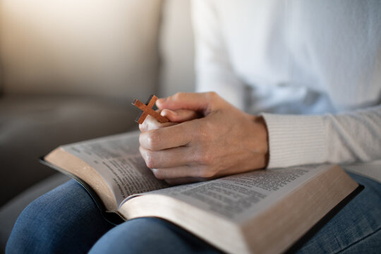 Woman praying with open Bible cross in hand at home, faith and devotion concept
