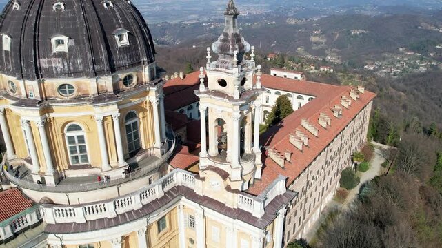 Aerial drone shot shows the majestic Basilica of Superga with its grand dome and monastery buildings on the hilltop in Turin, Italy, baroque architecture, urban panorama, sunny daylight scene.