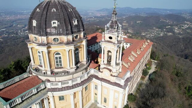 High angle drone shot shows the majestic Basilica of Superga with its grand dome and classical portico on the hilltop in Turin, Italy, historic baroque architecture, city panorama, sunny daylight.
