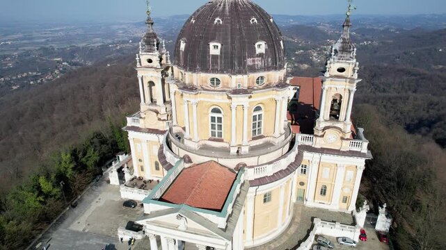 High angle drone shot shows the majestic Basilica of Superga with its grand dome and classical portico on the hilltop in Turin, Italy, historic baroque architecture, city panorama, sunny daylight.