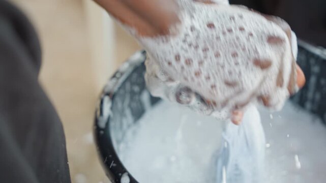 Scrubbing and rinsing cloth in bucket outdoors. Prolonged rinse sequence with hands and water outside home. Cleaning cloth outdoors with vigorous hand motions and water in continuous rinse process