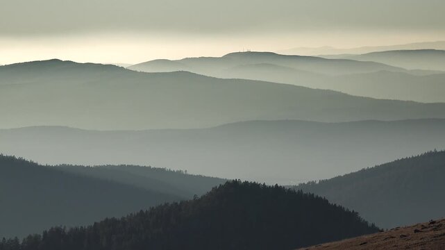 Panoramic view of afternoon light on successive forest covered ridges of the Pyrenees Mountains. Soft haze drifts through layered hills as muted sunlight shapes the expansive Pyrenees landscape.