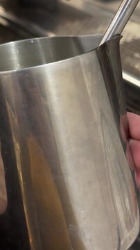 Astrakhan, Russia - January 16, 2025: Hand holding milk frothing pitcher with stainless steel