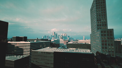 Fototapeta premium tower silhouette against distant skyline, moody teal tones and deep shadows create noir atmosphere, textured modern facade dominates foreground, cinematic drone