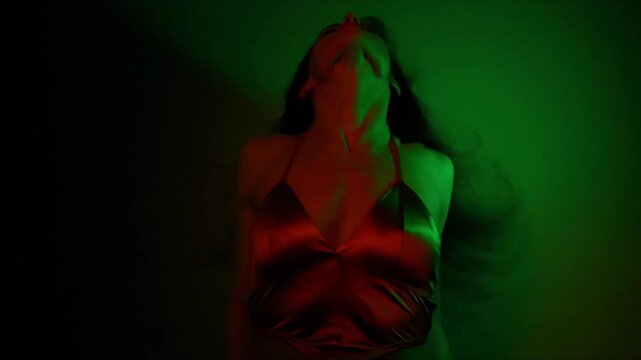 Sexy dancer woman with long hair dancing in a dark studio iridescent colorful light glows in fantasy club neon green orange rays. Magic blending light with body girl. Art creative expression video