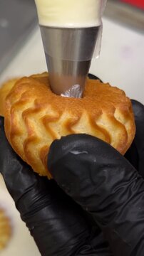 Baker decorates pastry with icing using piping bag in a kitchen setting