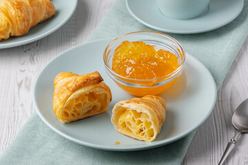 Croissant cut in half served with orange jelly on a blue plate with a spoon on a wooden table