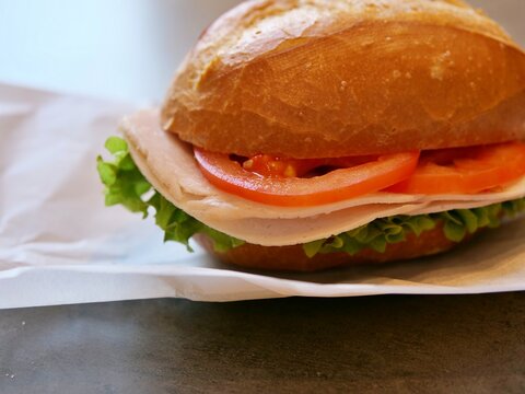 Freshly prepared crusty bread roll sandwich with ham, cheese, tomato,
and lettuce.
Close-up of a classic European-style breakfast or snack on white parchment
paper. delicious crusty bun filled 