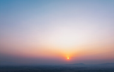 Fototapeta premium Sun setting over distant misty hills with pastel sky