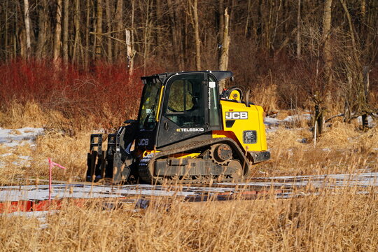 Yellow JCB Teleskid compact track loader working on ground protection mats in a rural construction site during autumn land clearing.