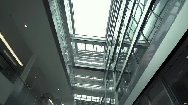 Bright multi level building atrium with glass walls and ceilings, steel structure and geometric lines creating a minimalist, airy interior with sky visible above
