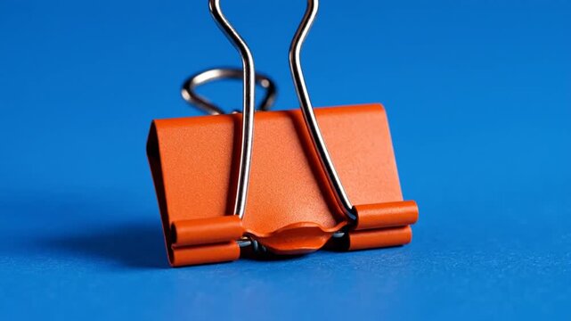 Close-up of an orange binder clip on a vibrant blue background, a common office supply.