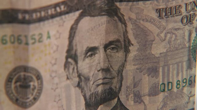 Close up of Abe Abraham Lincoln face on five 5 dollar cash paper bill in detail slo mo slow motion on green white text texture of American economy paperback financial bills of multiple dollars symbol