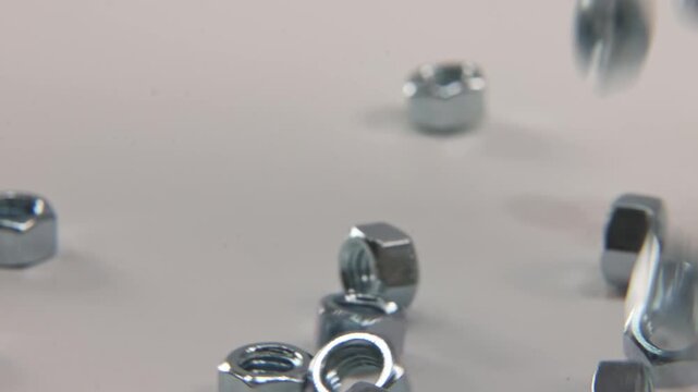 Slow motion close up of screw bolt imperial metric nuts that are silver, steel, and metal falling into place on white surface for industrial work in a tech technology electronics shop studio lighting