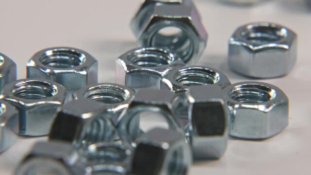 Slow motion close up of screw bolt imperial metric nuts that are silver, steel, and metal falling into place on white surface for industrial work in a tech technology electronics shop studio lighting