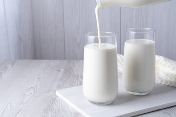 Pouring homemade kefir, buttermilk or yogurt with probiotics. Yogurt flowing from glass bottle on light background. Probiotic cold fermented dairy drink. Trendy food and drink. Copy space