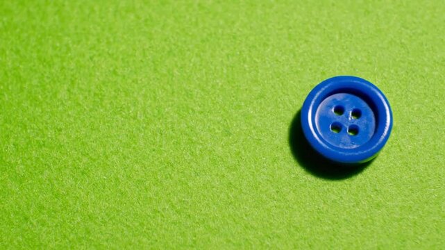 Close-up of a vibrant blue button with four holes, casting a shadow on a bright green textured surface, ideal for craft and sewing projects.