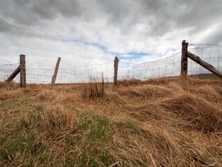Wooden fence and low cloudy sky. Nature scene in Irish country side with brown agriculture land.