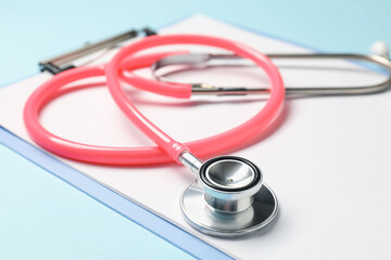 Stethoscope and clipboard on light blue background, closeup