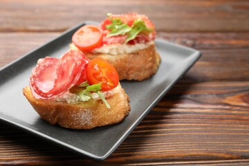Delicious bruschettas with salami sausage, cream cheese and tomatoes on wooden table, closeup. Space for text