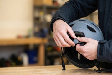 Obraz premium A man adjusts the fitting system on the back of a grey bicycle helmet for safety