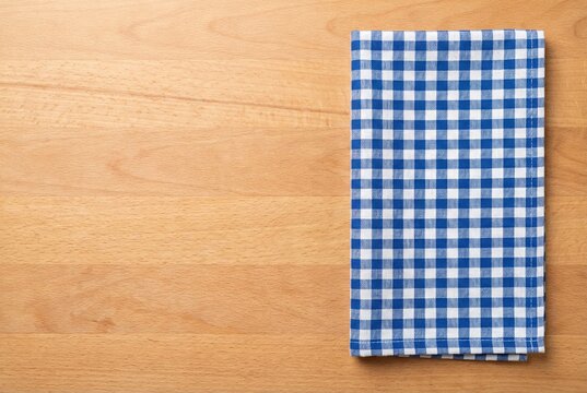 Folded blue and white gingham kitchen towel placed on the right edge of a light brown wooden table surface