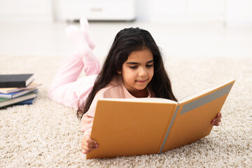 Fototapeta premium Cute little girl reading book on floor at home